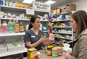Farmacéutica ayudando a una clienta con suplementos para mascotas AdvaMate en una tienda minorista.