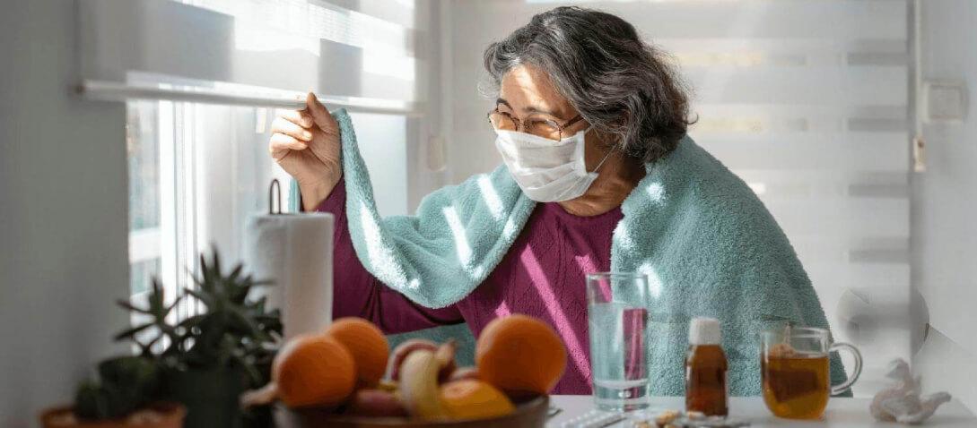 Woman with long COVID wearing a mask, looking out of the window. Woman with long COVID wearing a mask, looking out of the window.