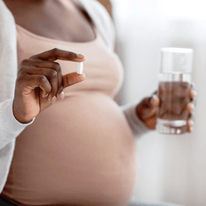 Una mujer embarazada está tomando una pastilla con minerales y vitaminas.